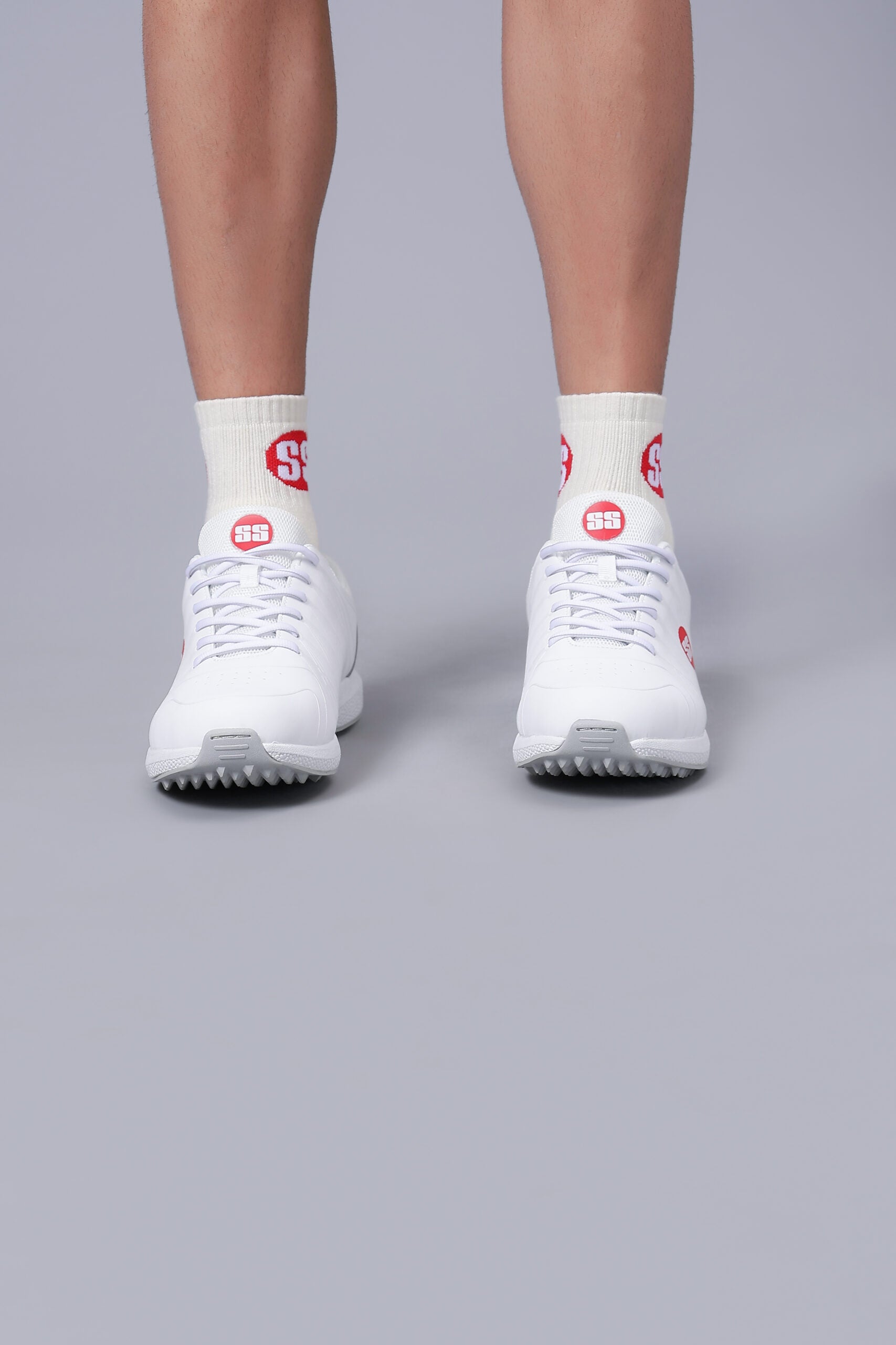 A pair of white cricket shoes with red detailing and socks SS TON White Edition cricket shoes with lightweight performance design